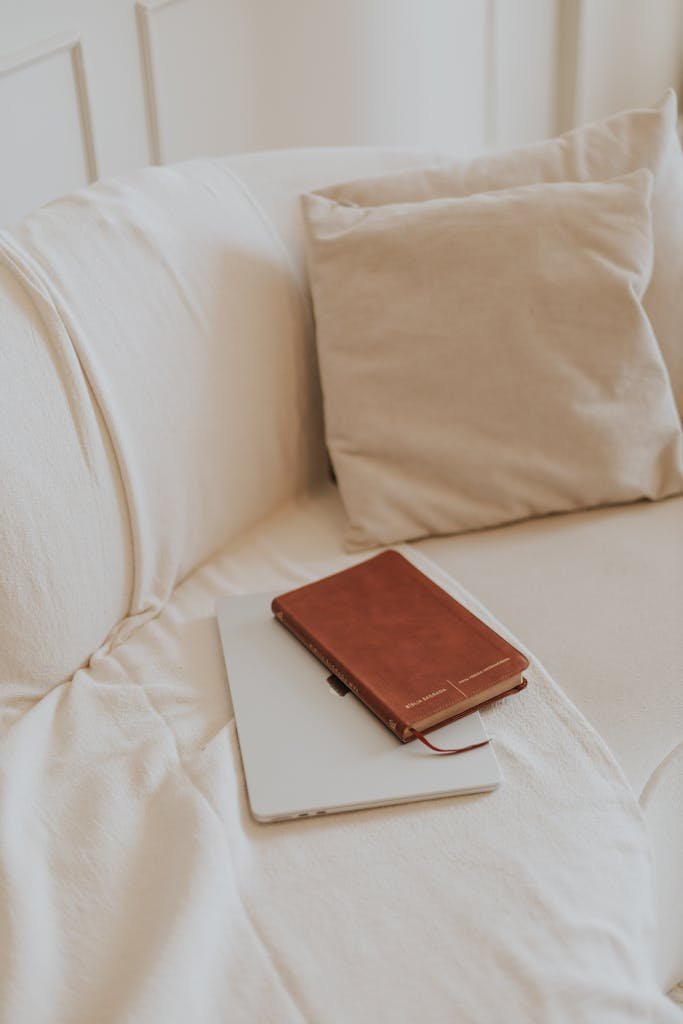 A leather notebook and tablet rest on a soft beige sofa, creating a calm and inviting reading nook.